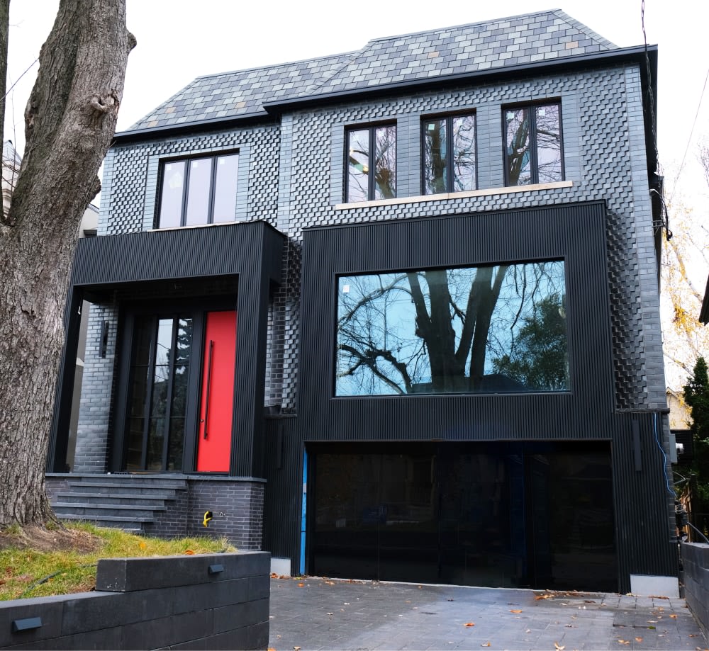 Exterior of house with black glazed brick and a red door.