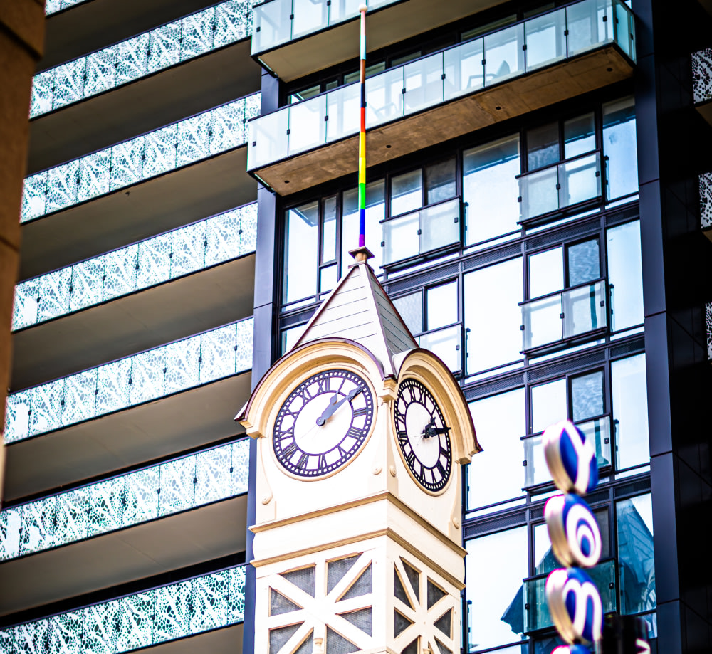 Top of clock tower with white brick and a pole with pride flag.