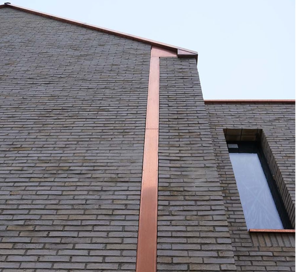 Exterior corner of house with beige brick and metallic detail.