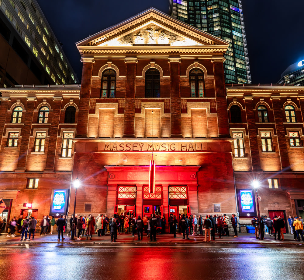 Front of Massey Hall lit up at night with lights.