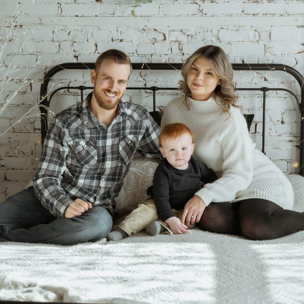 Mom, dad, toddler boy sitting on bed.