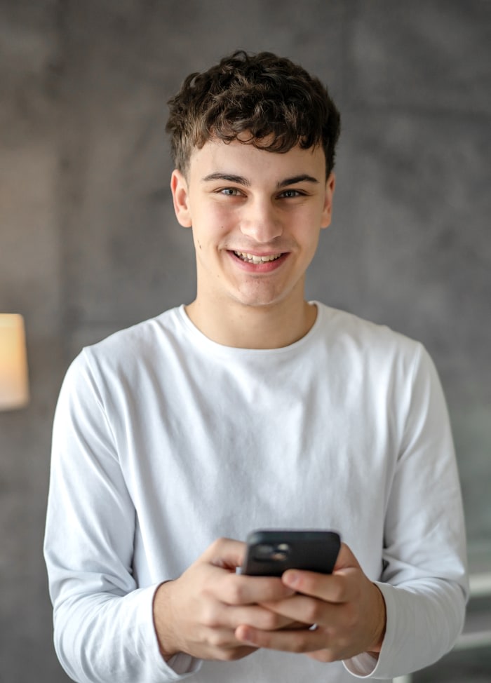 A young teen boy smiling and posing while using his cellphone.
