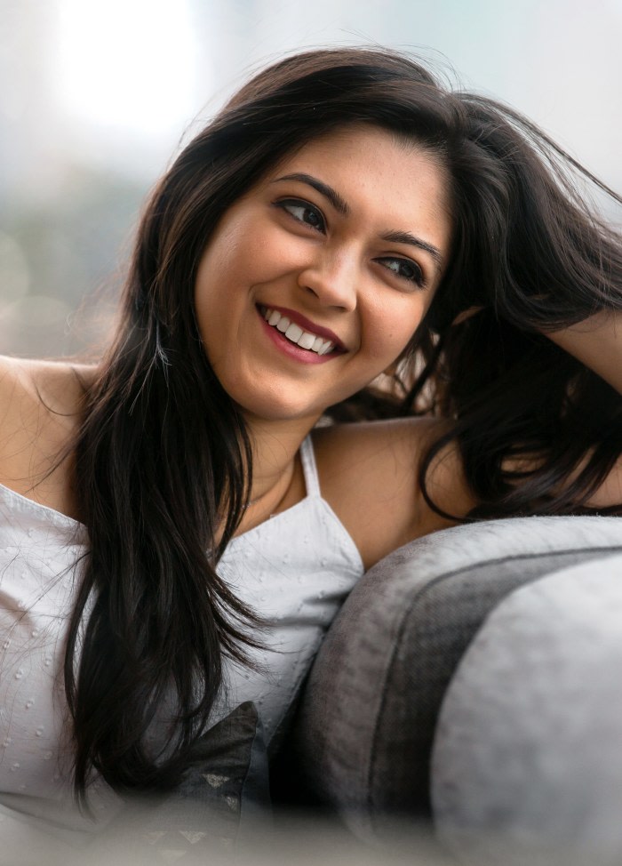 A woman with long dark hair is leaning over the back of a sofa.