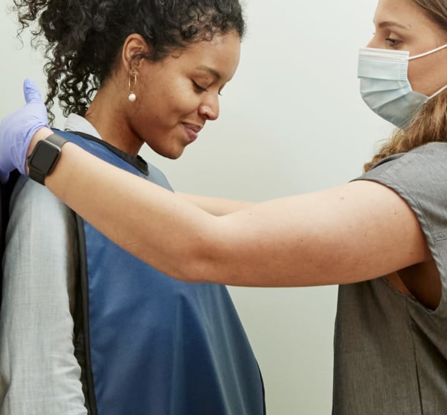 Dental professional placing protective X-ray bib over patient.