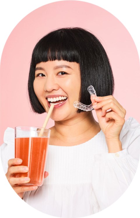 A woman is drinking a red drink and holding clear aligners.