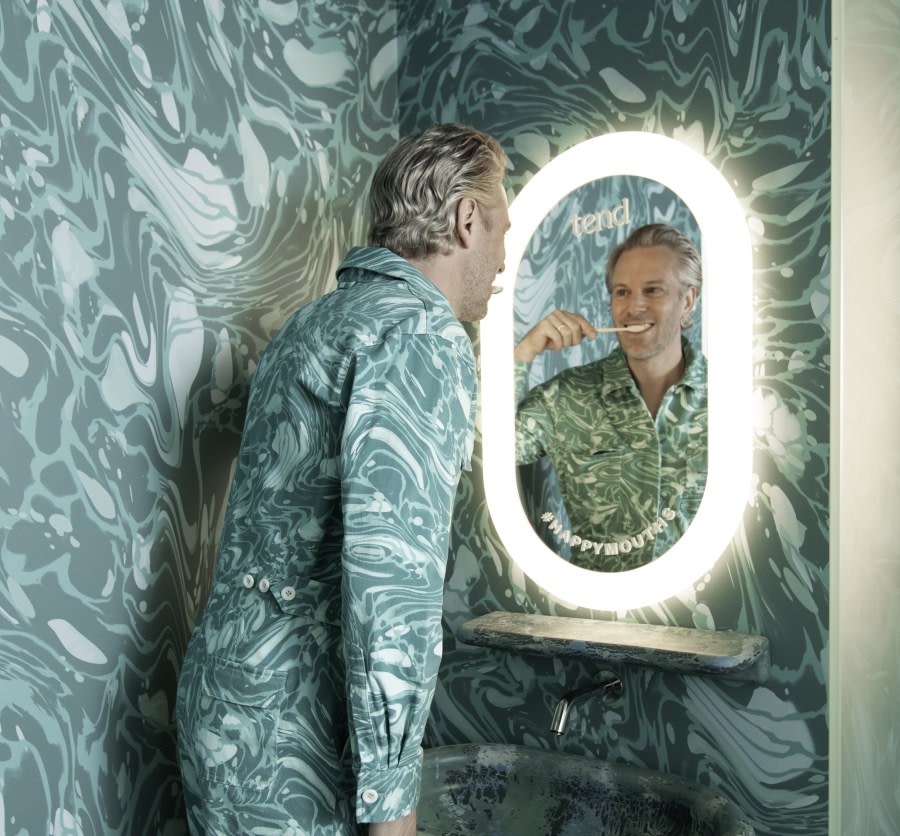 A man brushes his teeth in an outfit that matches the walls.