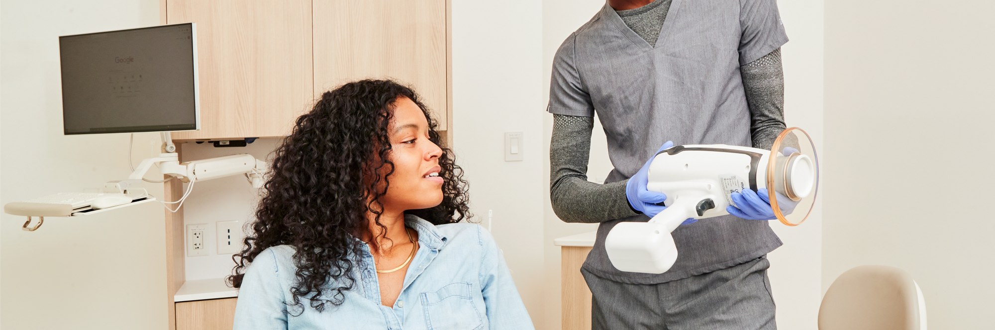 Dental professional showing portable X-ray machine to patient.