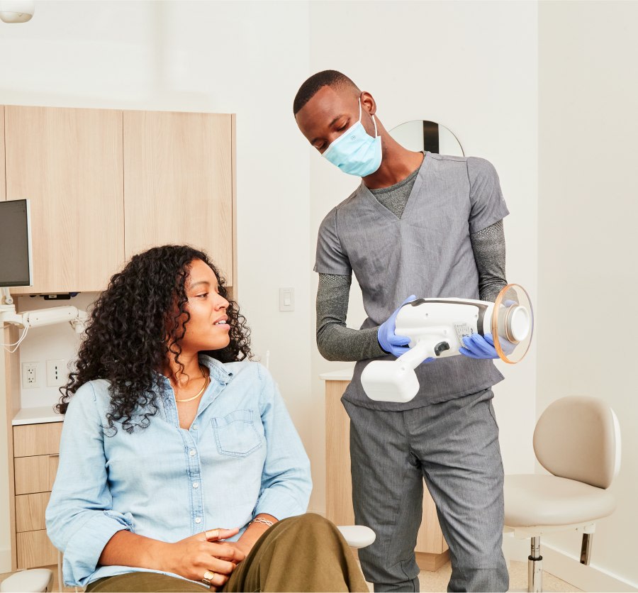 Dental professional showing portable X-ray machine to patient.