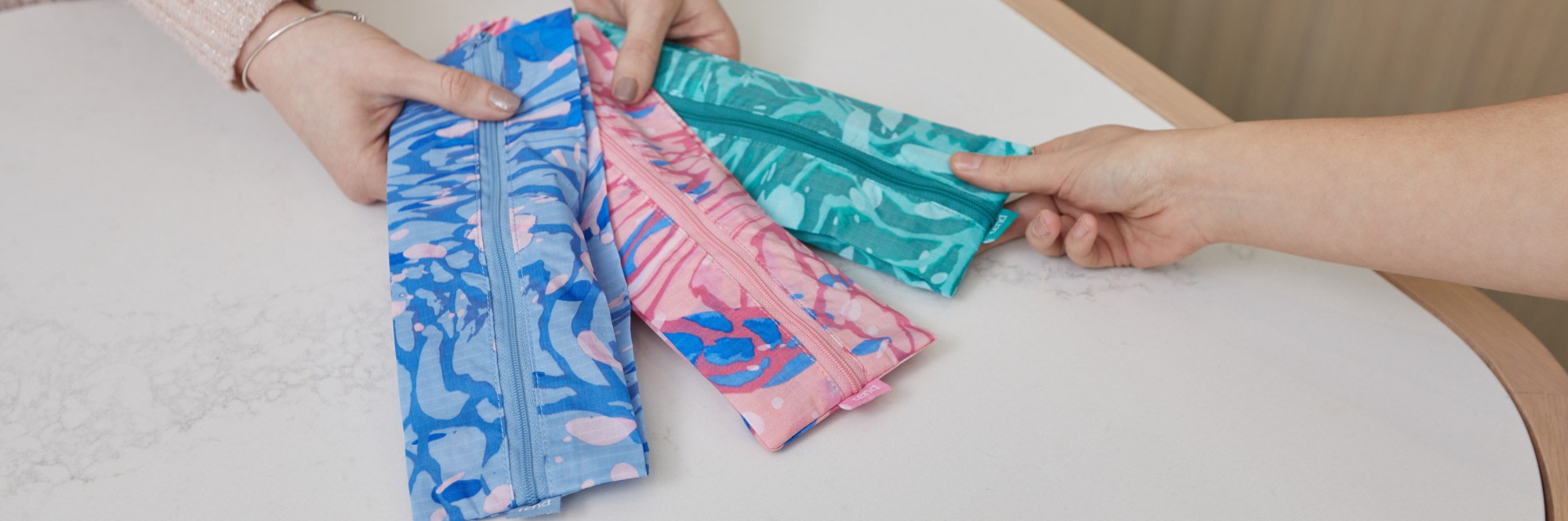 Hands holding out a pink, green and blue brush bags for patient.
