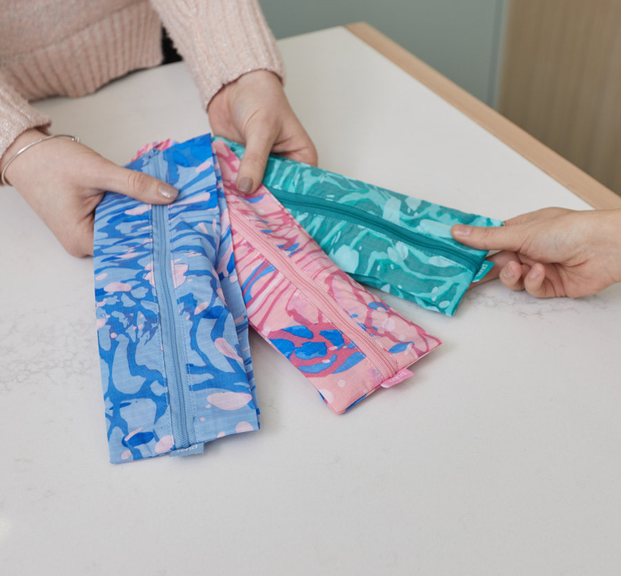 Hands holding out a pink, green and blue brush bags for patient.