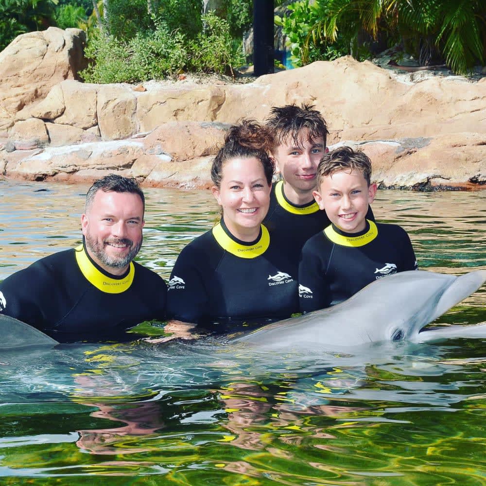 Mom, dad, two teeanage boys in a pool with a dolphin