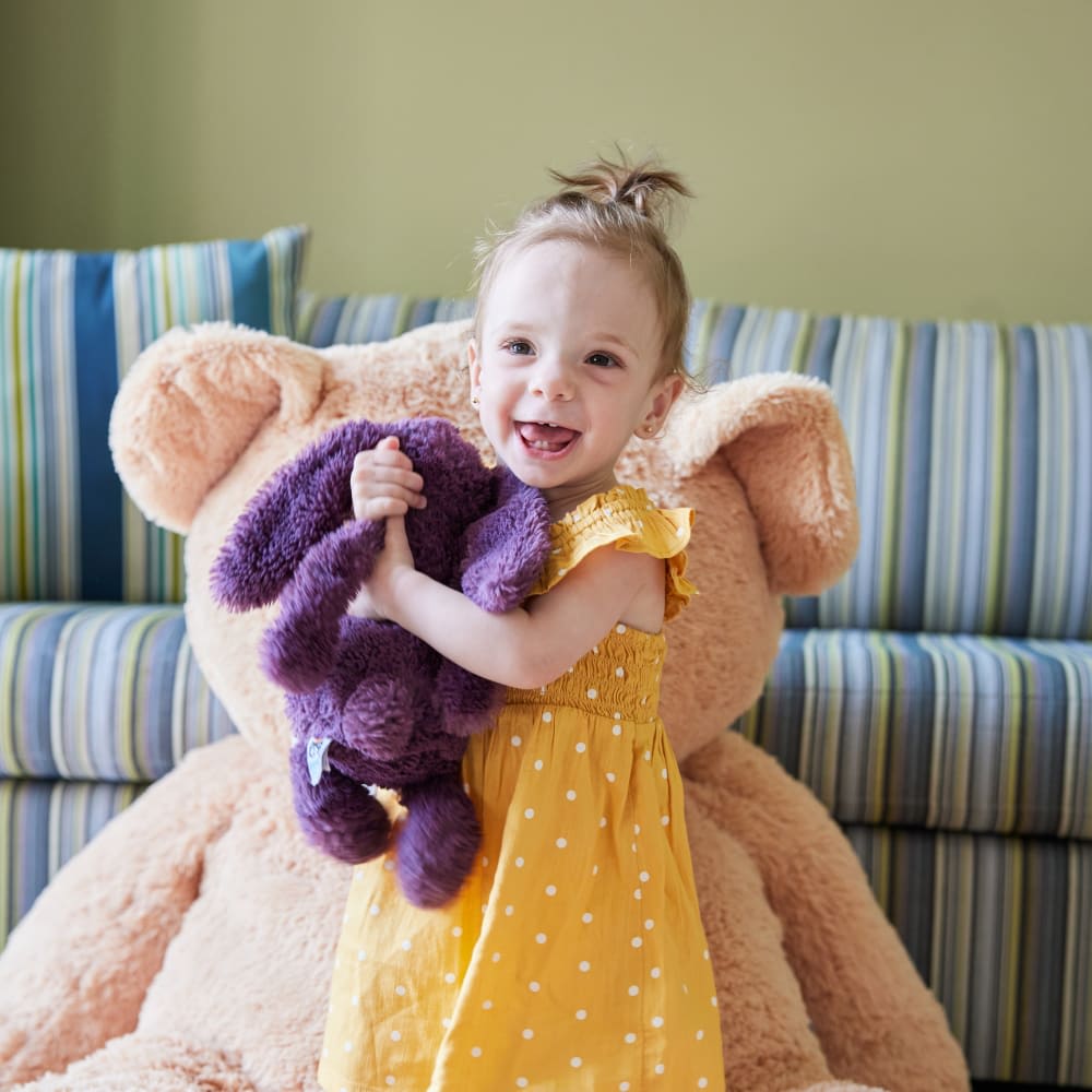 Toddler girl hugging purple stuffed animal.