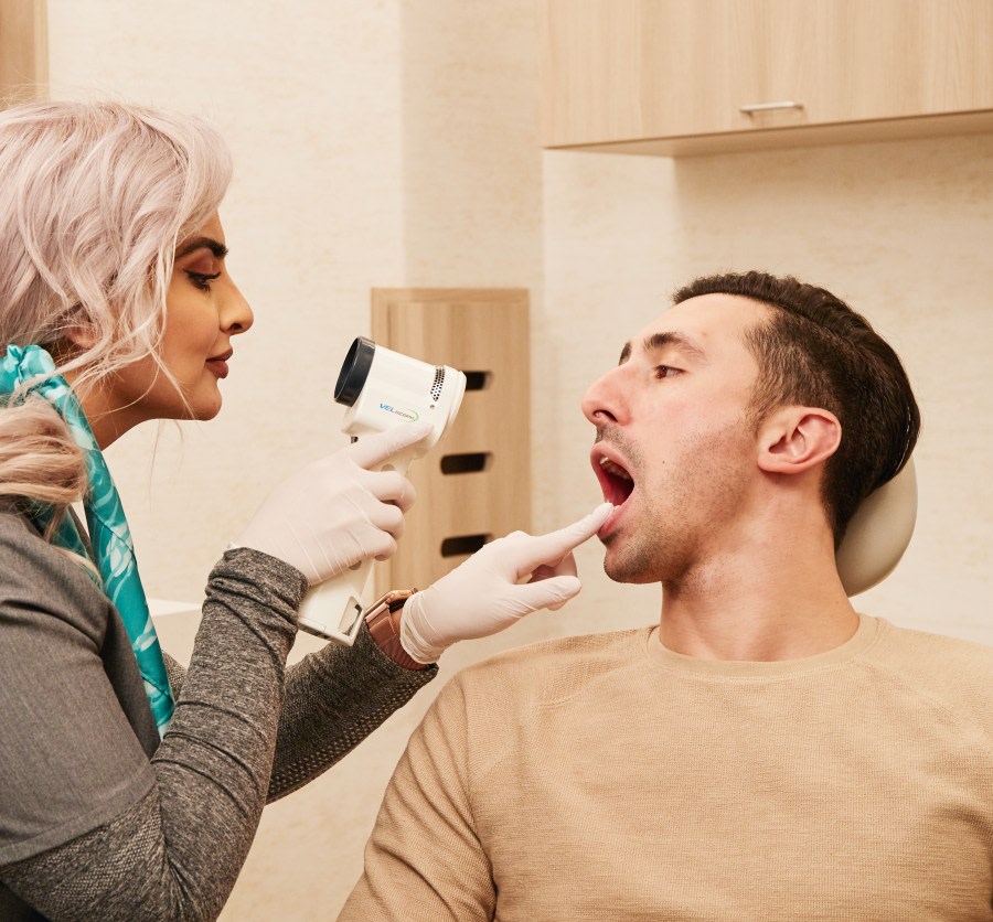 A team member looks in a patient's mouth with a VELscope.