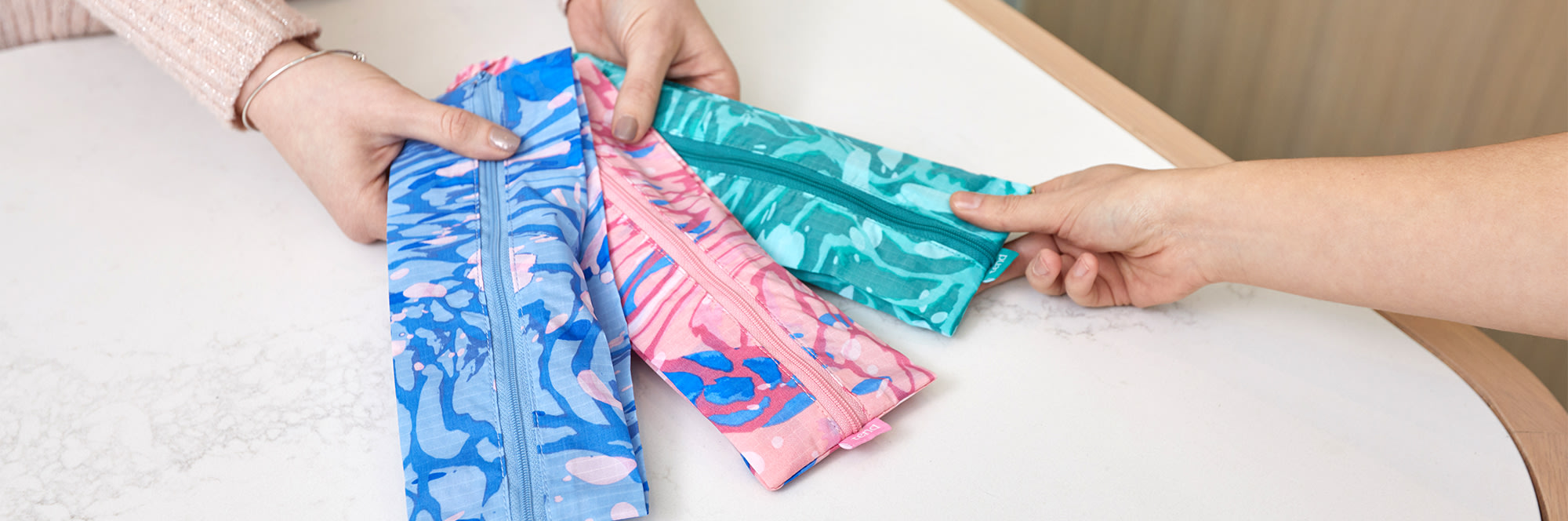 Hands holding out a pink, green and blue brush bags for patient.