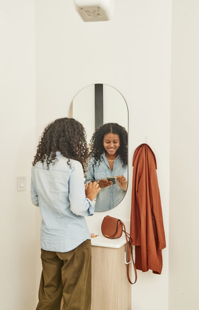 A patient stands in front of a mirror and uses her phone.