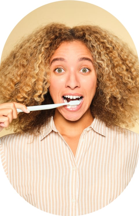 A lady with curly hair brushes her teeth.