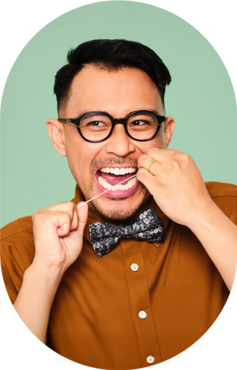 A man with round glasses is flossing his teeth.