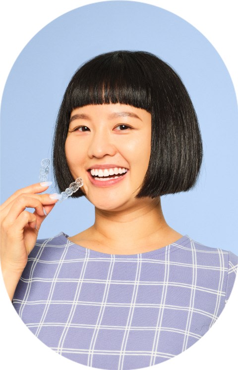 A woman with a short bob hairstyle is holding clear aligners.