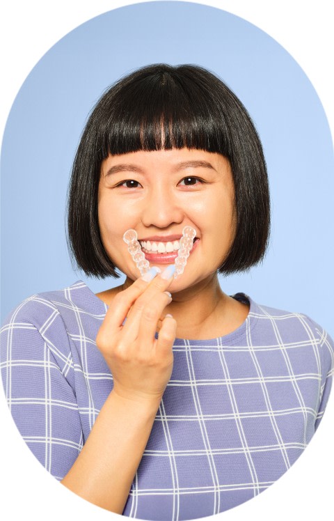 A woman is holding clear aligners up to his mouth.