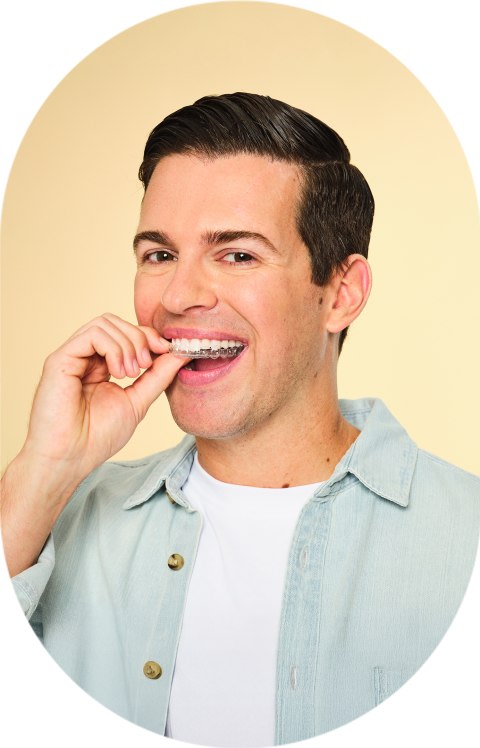 A man is holding clear aligners up to his mouth.