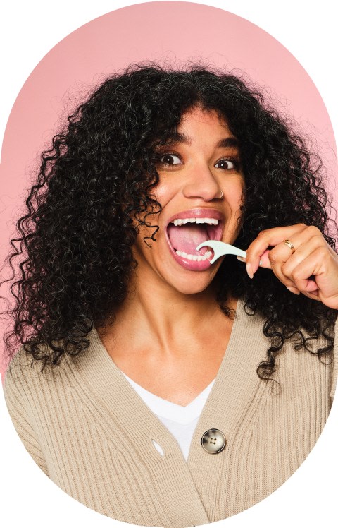 A woman with curly hair is flossing her teeth.