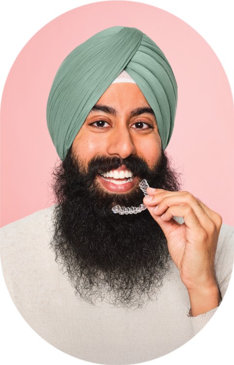 A man with a large beard holds clear aligners up to his mouth.