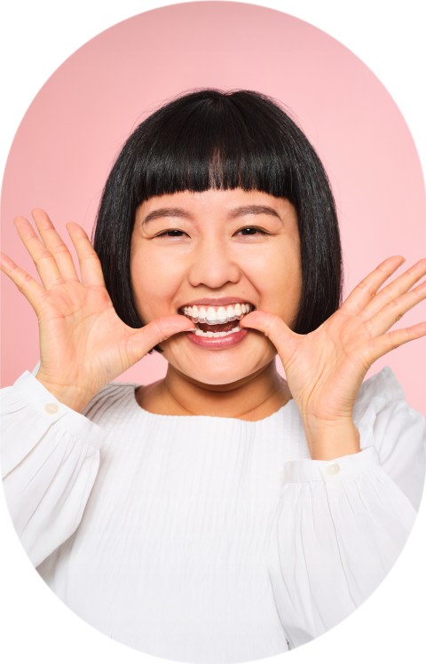 A woman with a short bob hairstyle is putting in clear aligners.