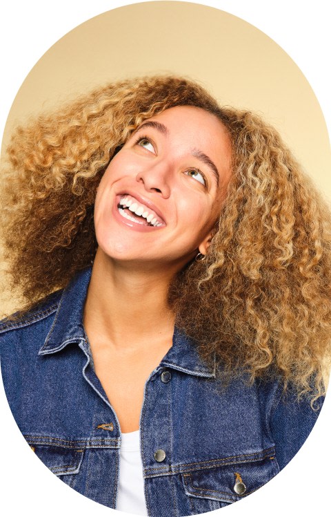 A woman with curly hair is smiling and looking up.
