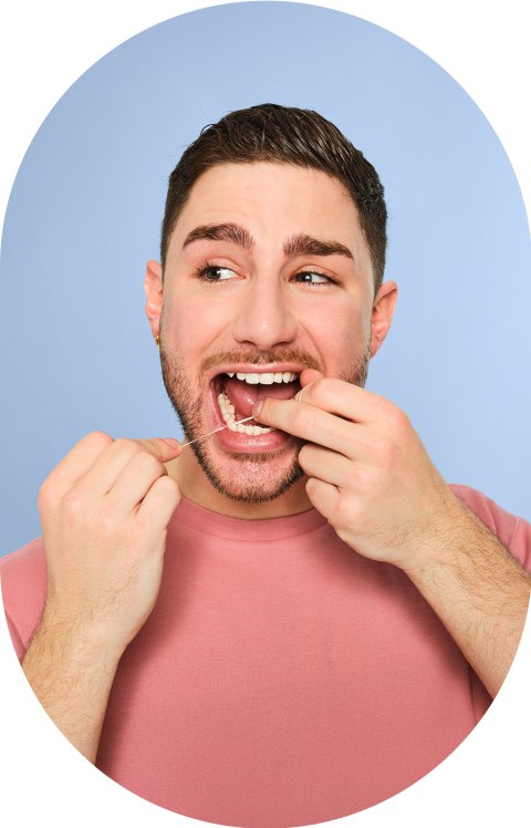A man in a pink shirt is flossing his teeth.