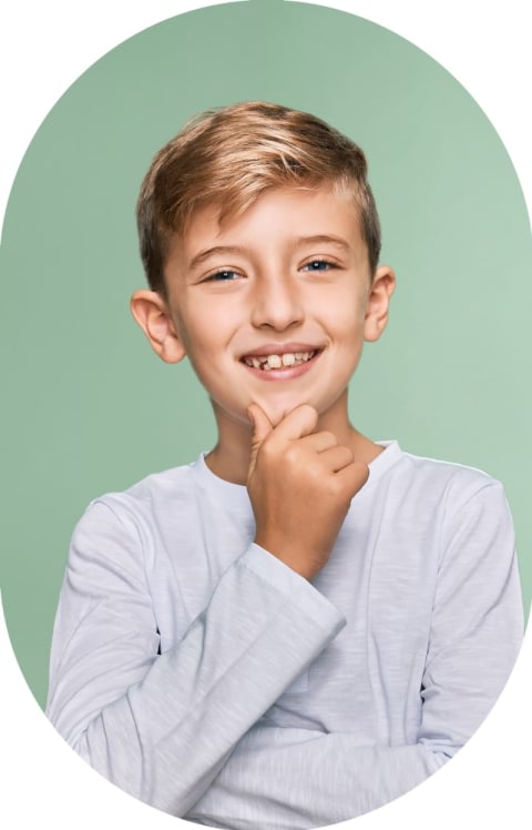 A kid in a white shirt is smiling. His hand is on his chin.
