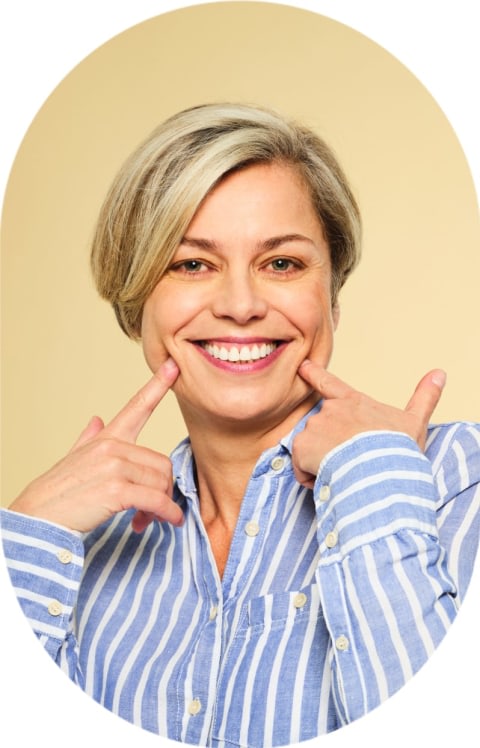 A woman points at her smile with two fingers.
