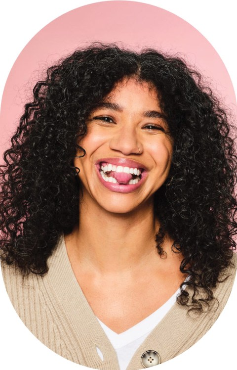 A woman with curly hair is smiling and sticking out her tongue.