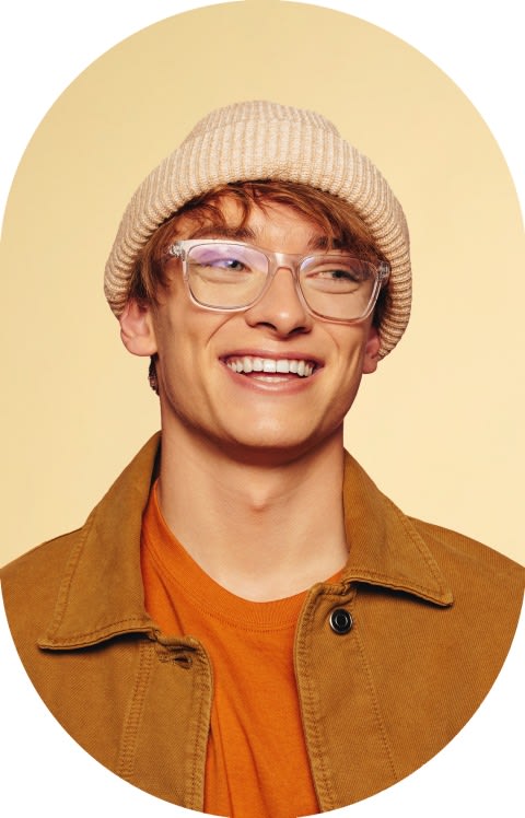 A young man in a hat and glasses is smiling.