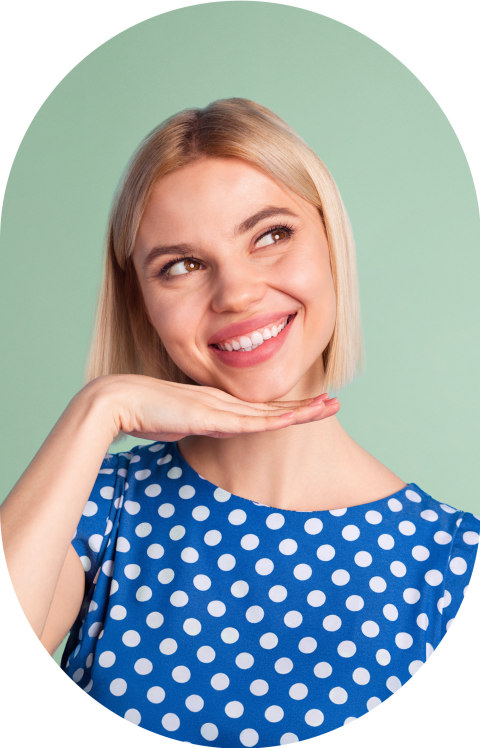 A woman in a blue short is smiling. Her hand is under her chin.