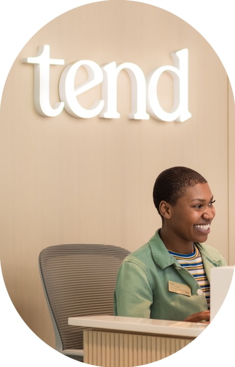 A Tend employee is sitting at a reception desk smiling.